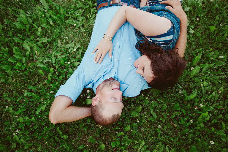 engaged couple wears blue cuddles on grass in Edmonton