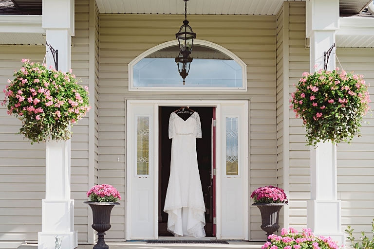 Stunning wedding dress with sleeves hangs in the bride's doorway prior to her University of Alberta wedding with a . Faculty Club reception in Edmonton